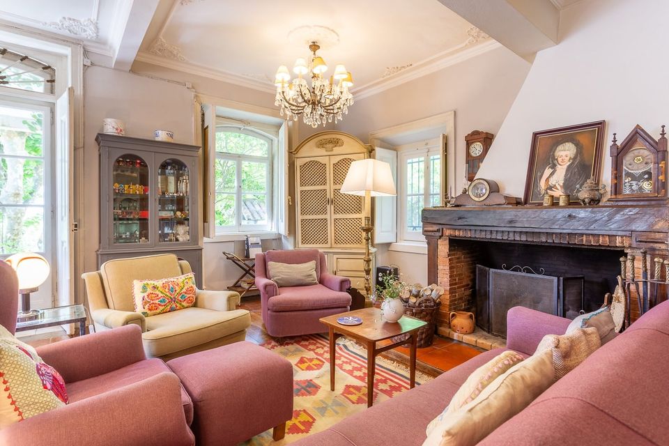 The living room: a chandelier, an open fireplace, dusty-pink armchairs and sofas grouped on a patterned rug.