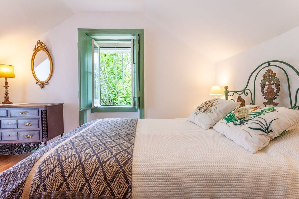 The Green Room: a bed with a painted iron headboard beside a green-framed window opening onto the trees.