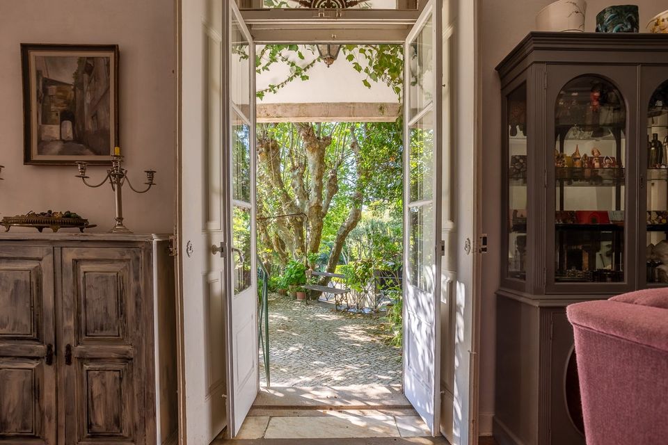 Double doors standing open from the house onto the garden, an antique cabinet to one side and greenery beyond.