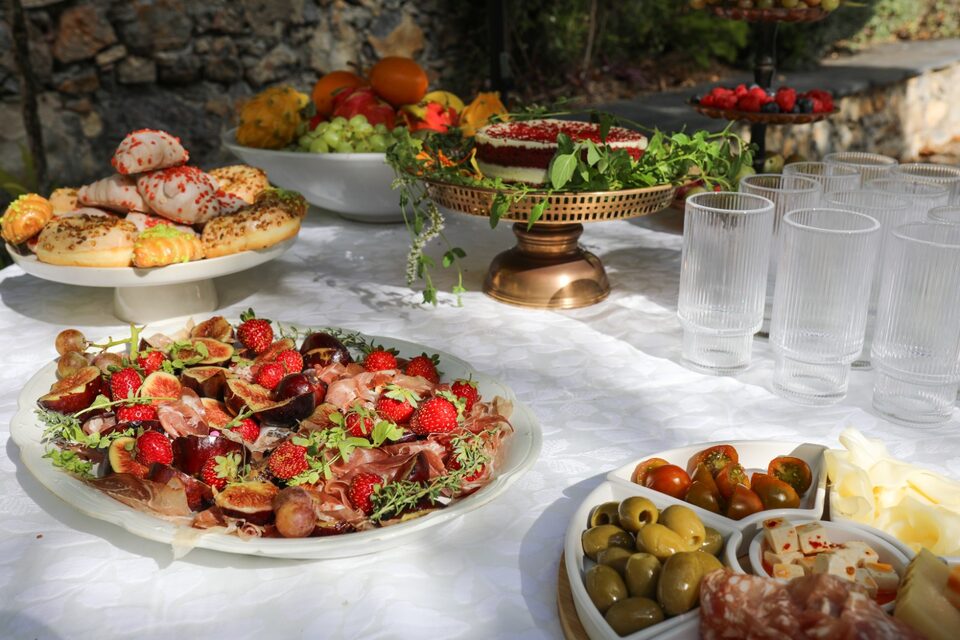 A caterer&rsquo;s table in the garden: figs and prosciutto with strawberries and thyme, pastries, olives and cheese, and a red velvet cake on a brass stand.