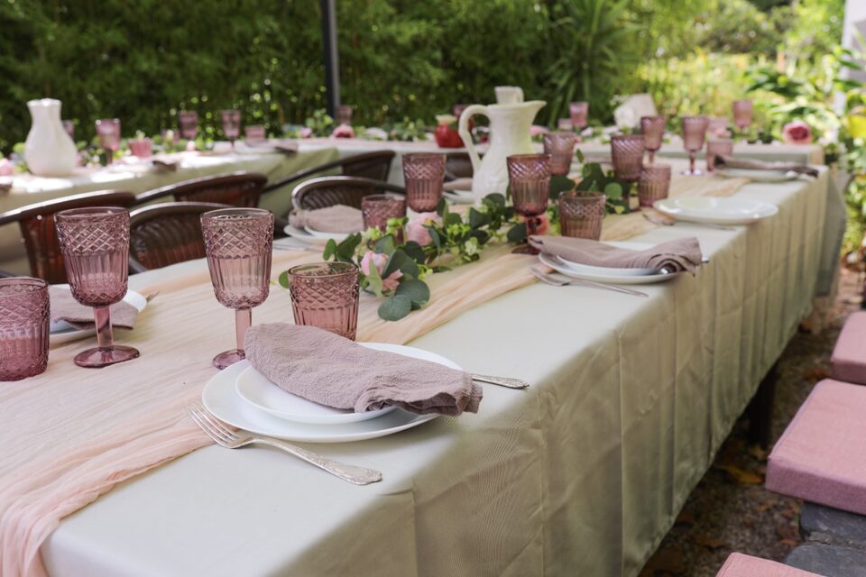 The long table seen down its whole length, set with rose-coloured glasses, a blush runner and a garland of eucalyptus and roses running down the middle.